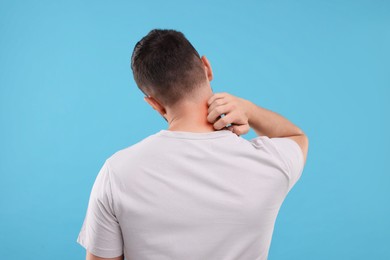 Photo of Allergy symptom. Man scratching his neck on light blue background, back view