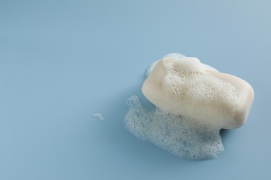 Photo of Soap bar with fluffy foam on light blue background, space for text