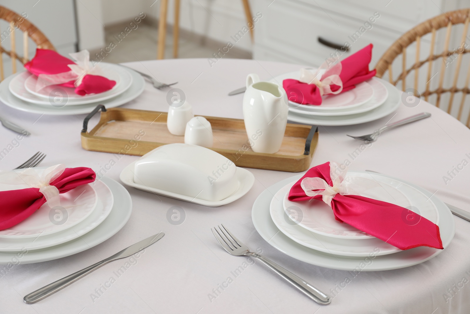 Photo of Color accent table setting. Plates, cutlery and pink napkins in dining room