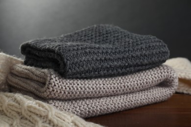 Photo of Knitted scarfs on wooden table against gray background, closeup