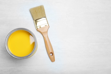 Photo of Can with yellow paint and brush on light background, top view. Space for text