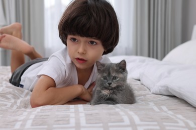 Photo of Cute little boy with kitten on bed at home. Childhood pet
