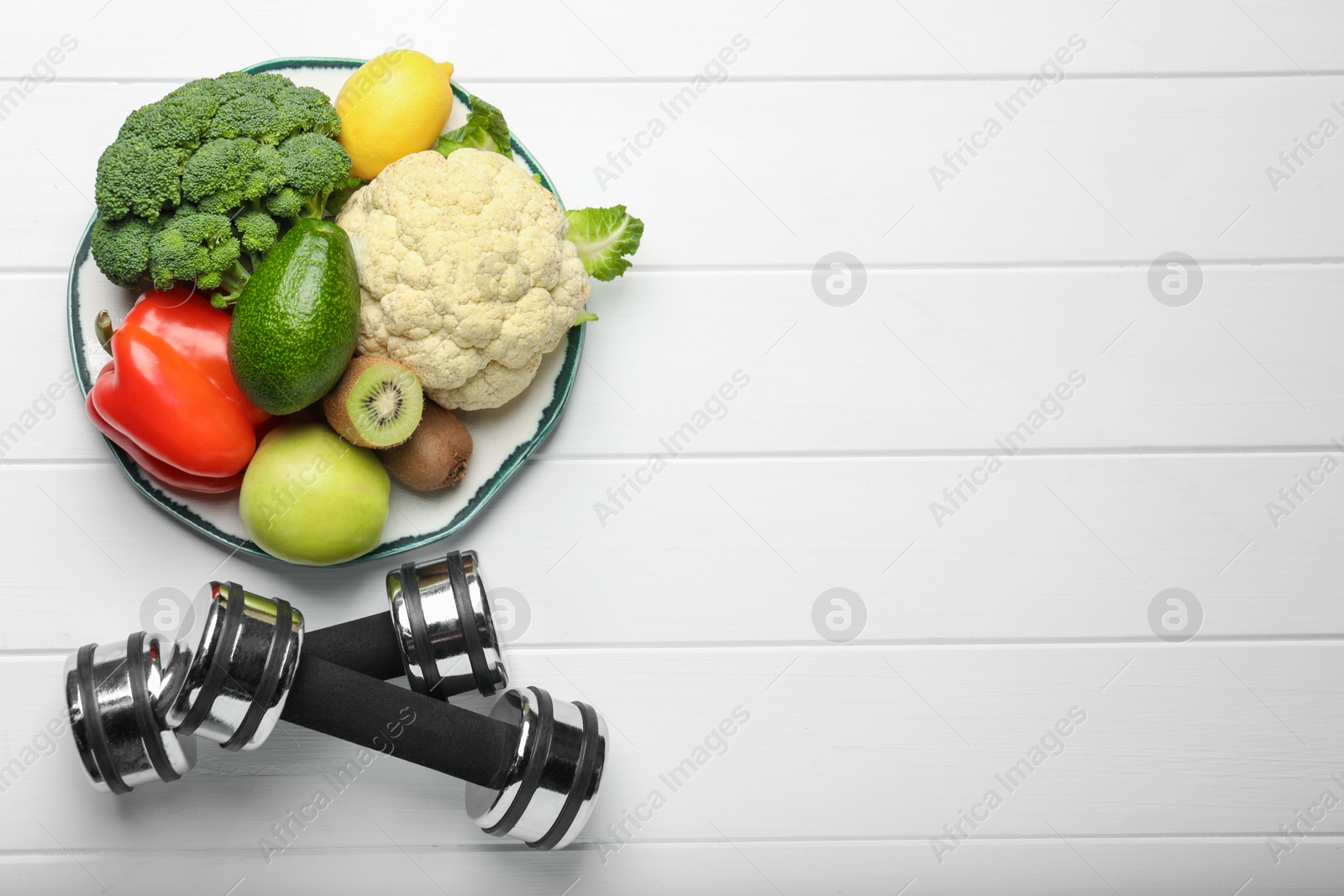 Photo of Healthy diet. Plate with products and dumbbells on white wooden table, flat lay. Space for text