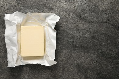 Block of tasty butter in open foil packaging on grey table, top view