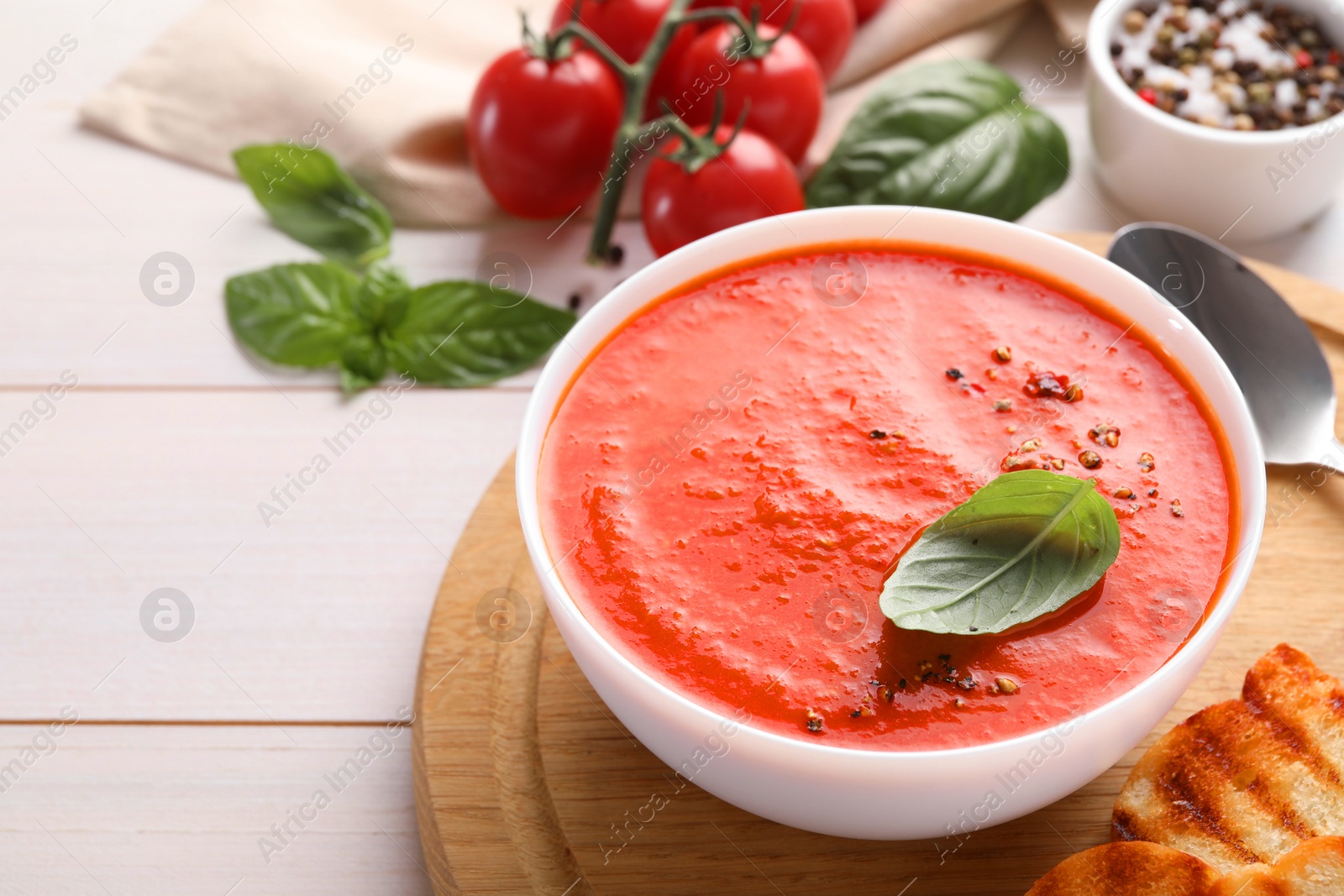 Photo of Delicious tomato soup served on white wooden table, space for text