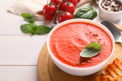 Photo of Delicious tomato soup served on white wooden table, space for text