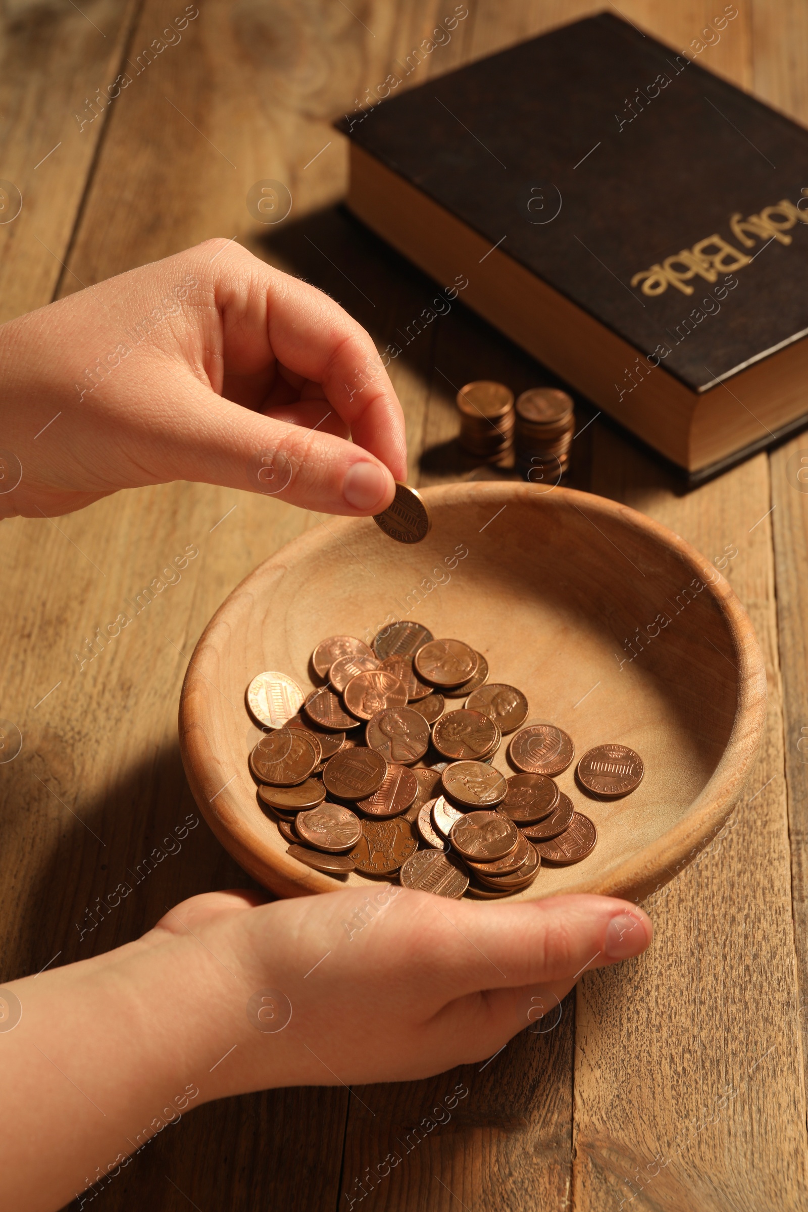 Photo of Donate and give concept. Woman putting coin into bowl at wooden table, closeup