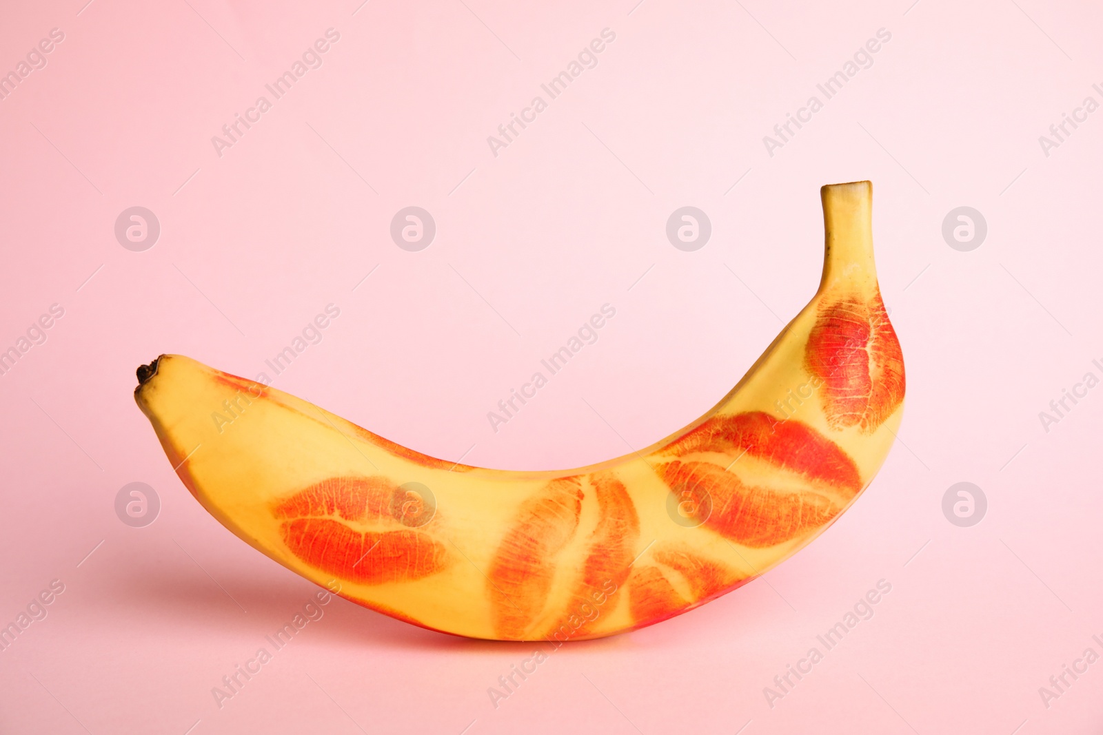 Photo of Fresh banana with red lipstick marks on pink background. Oral sex concept