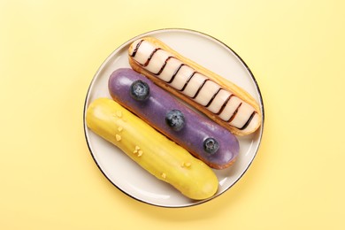 Photo of Delicious eclairs covered with glaze on yellow background, top view