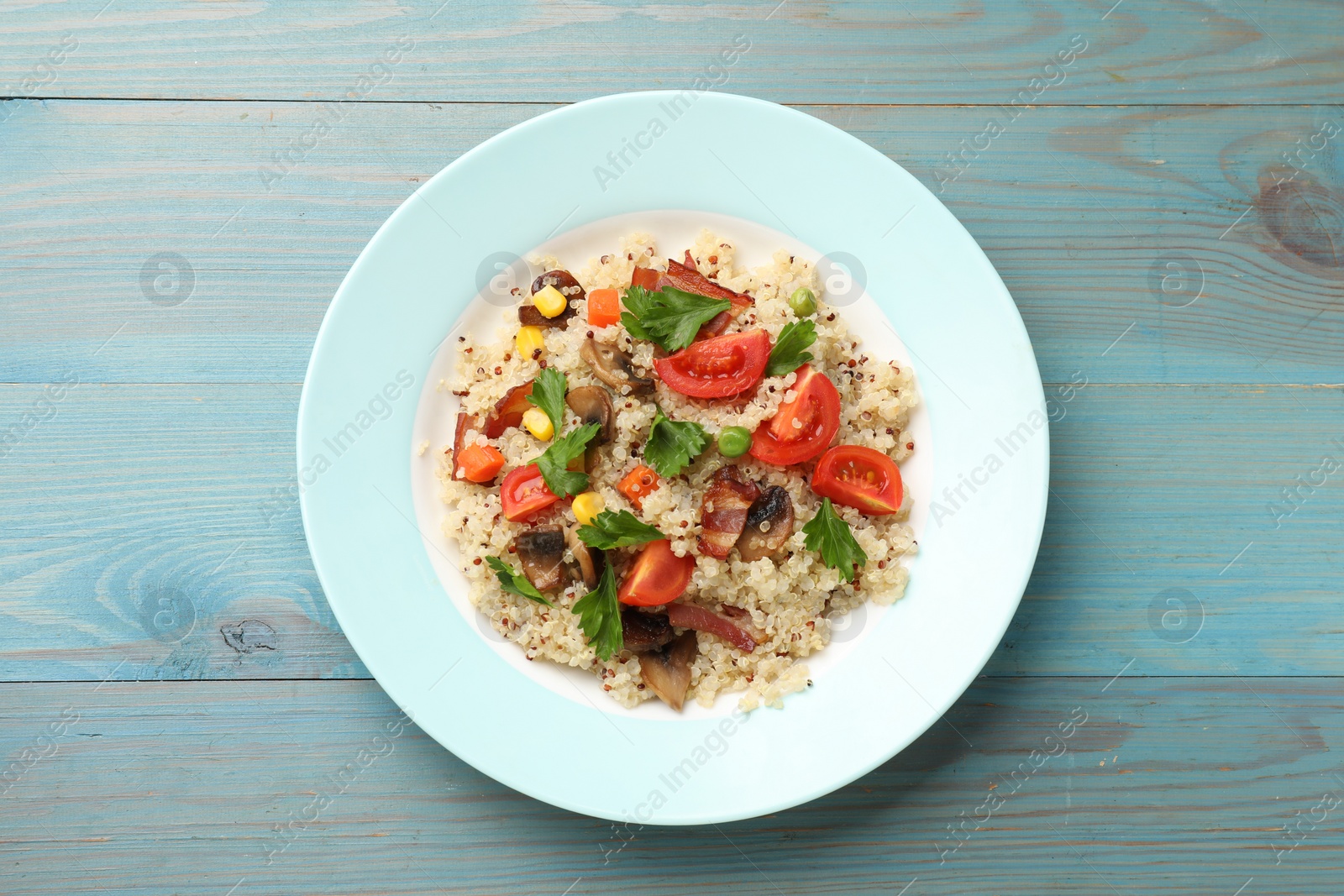 Photo of Plate of tasty quinoa porridge with fried bacon, mushrooms and vegetables on light blue wooden table, top view