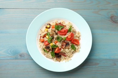 Photo of Plate of tasty quinoa porridge with fried bacon, mushrooms and vegetables on light blue wooden table, top view