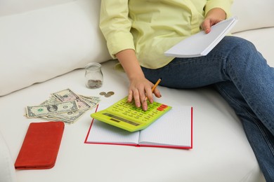 Photo of Young woman counting money with calculator on sofa indoors, closeup