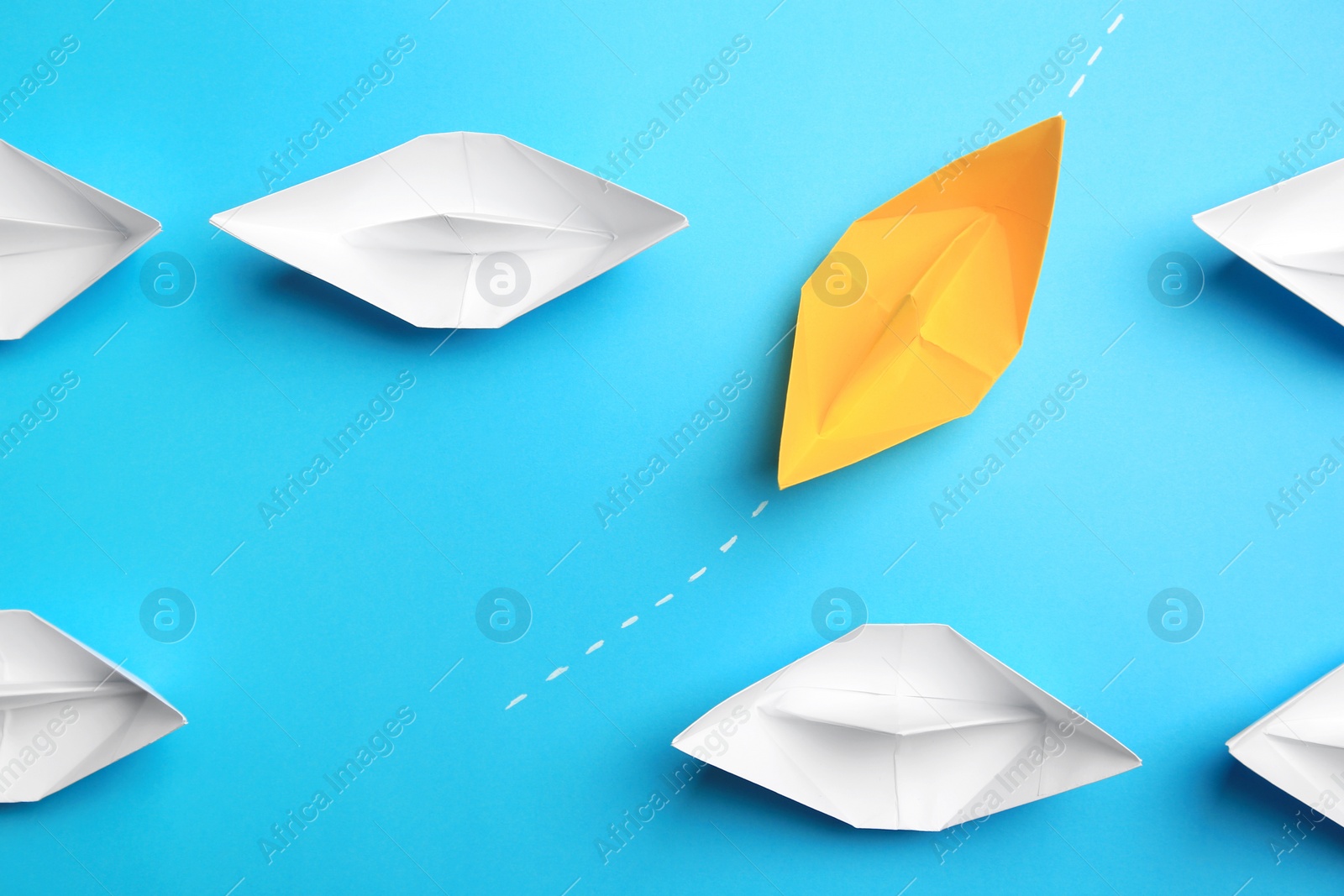 Photo of Yellow paper boat floating through others on light blue background, flat lay. Uniqueness concept