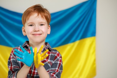 Little boy with painted hands near Ukrainian flag, space for text. Love Ukraine concept