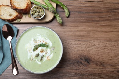 Photo of Delicious asparagus soup with pumpkin seeds served on wooden table, flat lay. Space for text