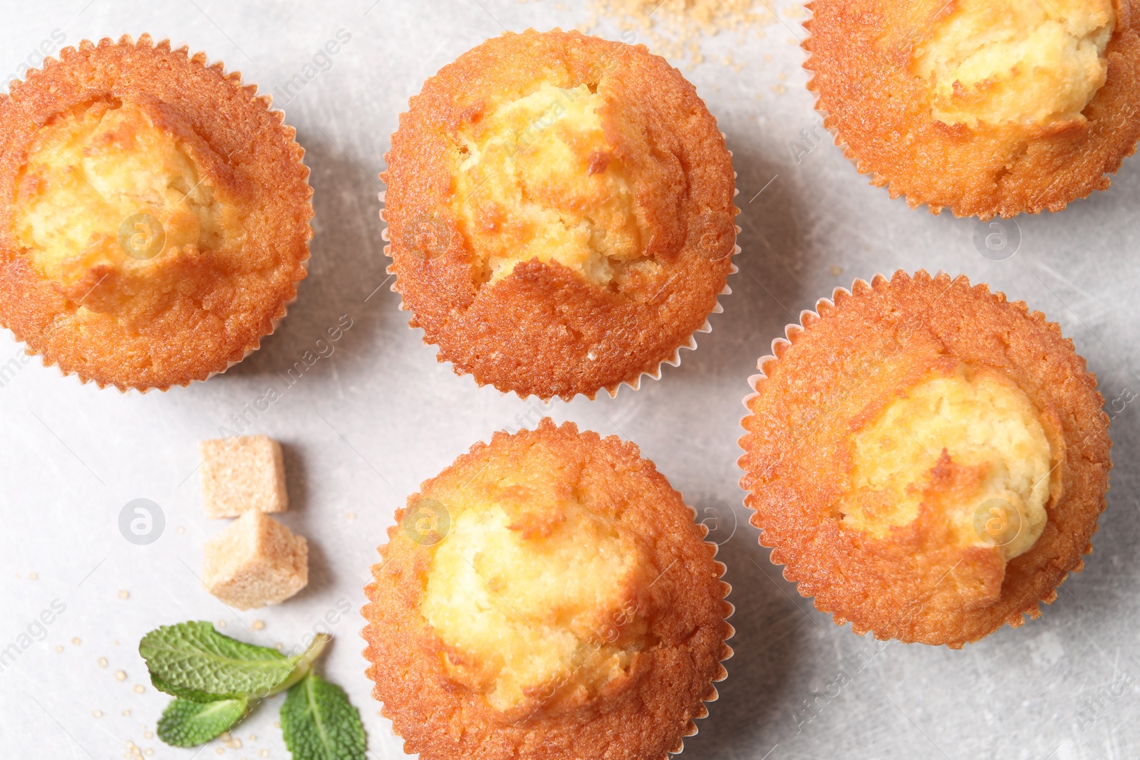 Photo of Delicious sweet muffins and brown sugar on light grey textured table, flat lay