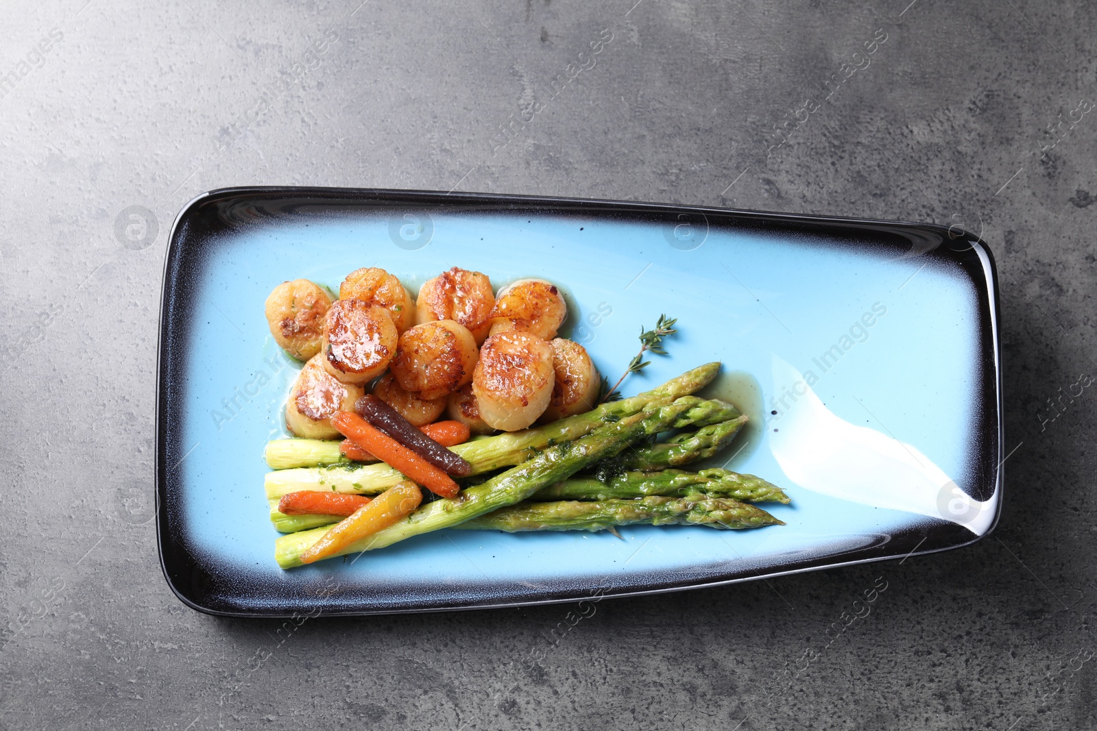 Photo of Delicious fried scallops with asparagus and vegetables on grey table, top view