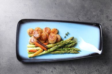 Photo of Delicious fried scallops with asparagus and vegetables on grey table, top view