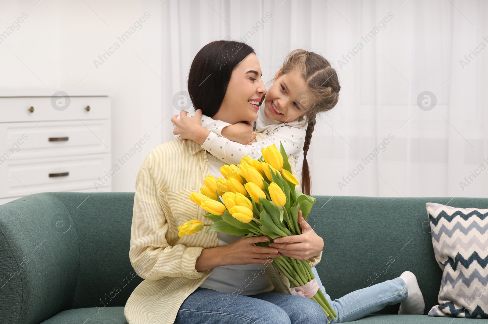 Photo of Happy woman and her cute daughter with bouquet of yellow tulips on sofa at home. Mother's day celebration