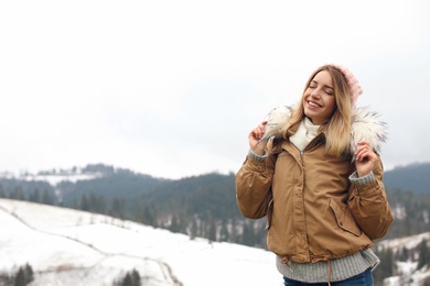 Photo of Young woman in warm clothes near snowy hill, space for text. Winter vacation