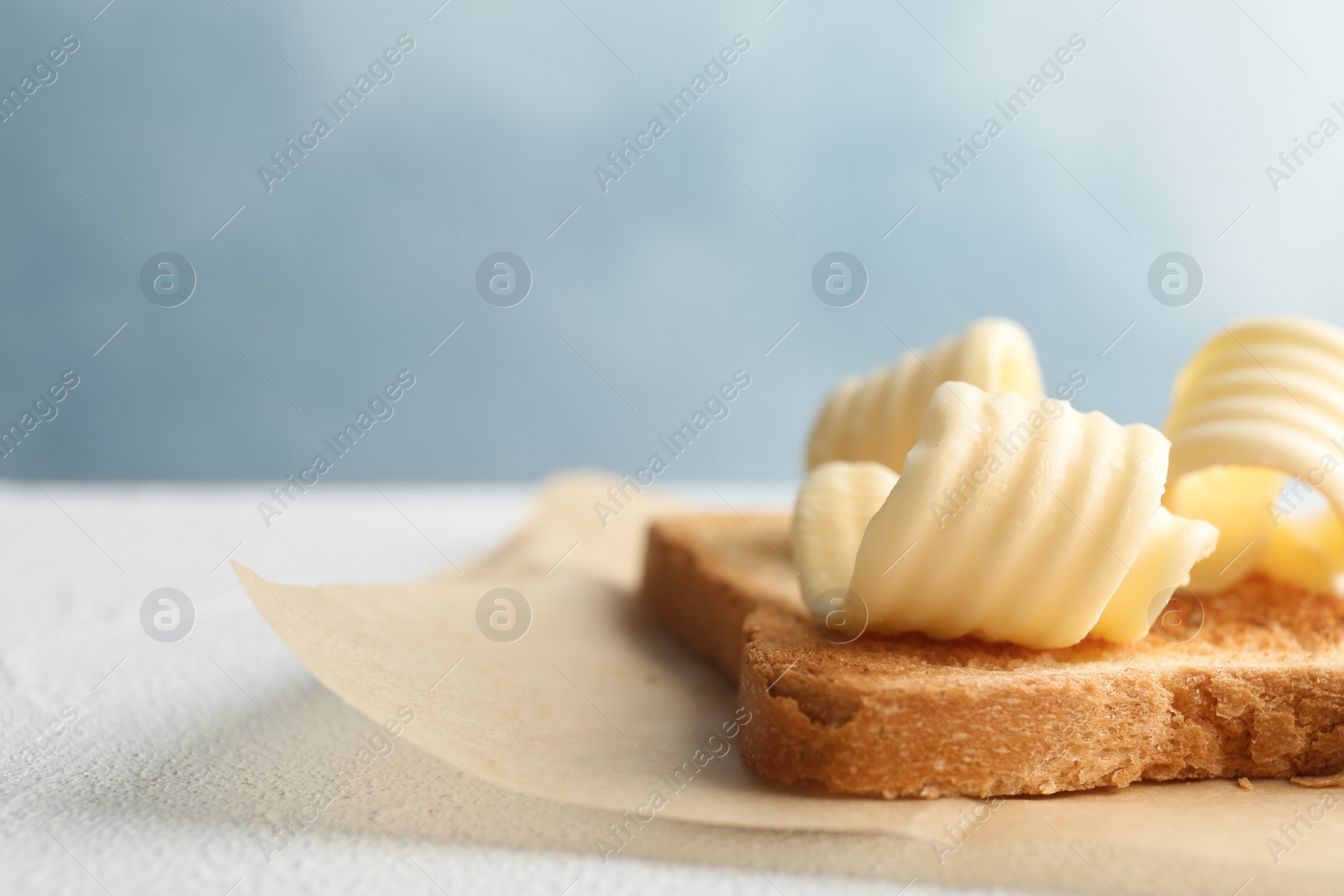 Photo of Toasted bread with fresh butter curls on table, closeup