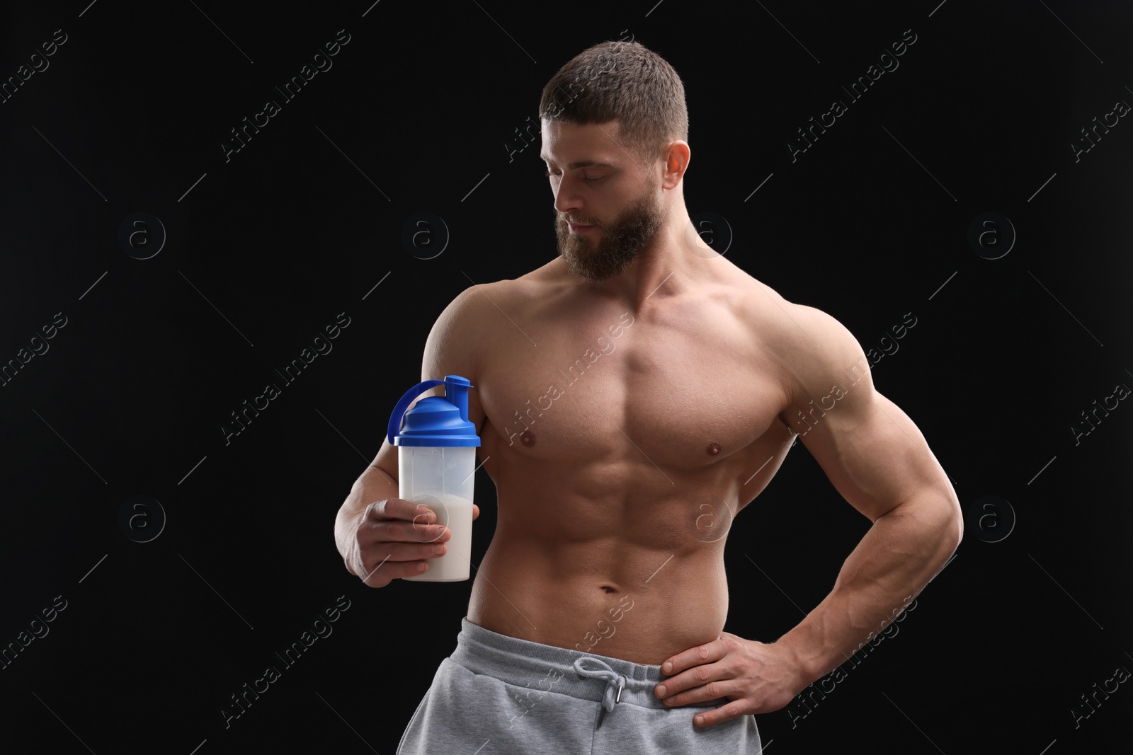 Photo of Young man with muscular body holding shaker of protein on black background