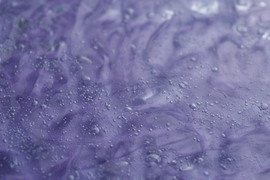 Photo of Texture of transparent shower gel on violet background, closeup