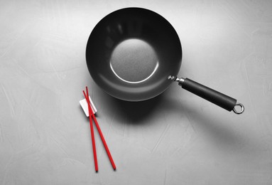 Empty iron wok and chopsticks on grey table, flat lay