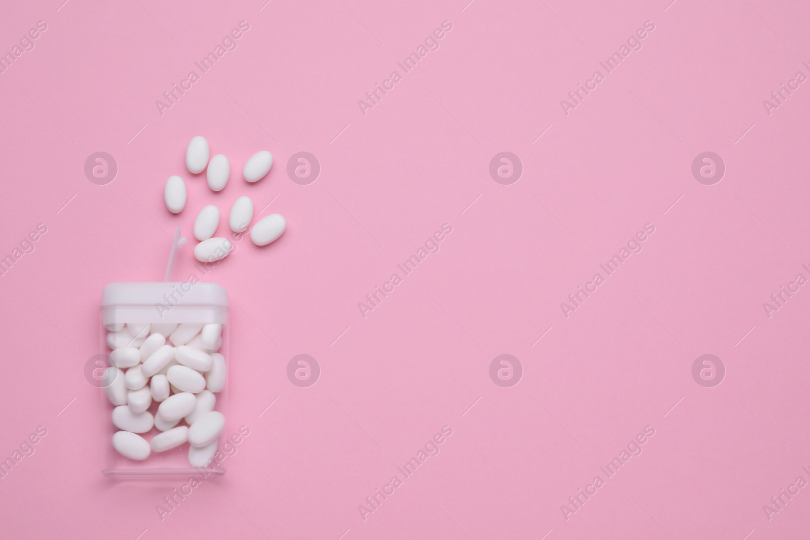 Photo of Tasty dragee candies and container on pink background, flat lay. Space for text