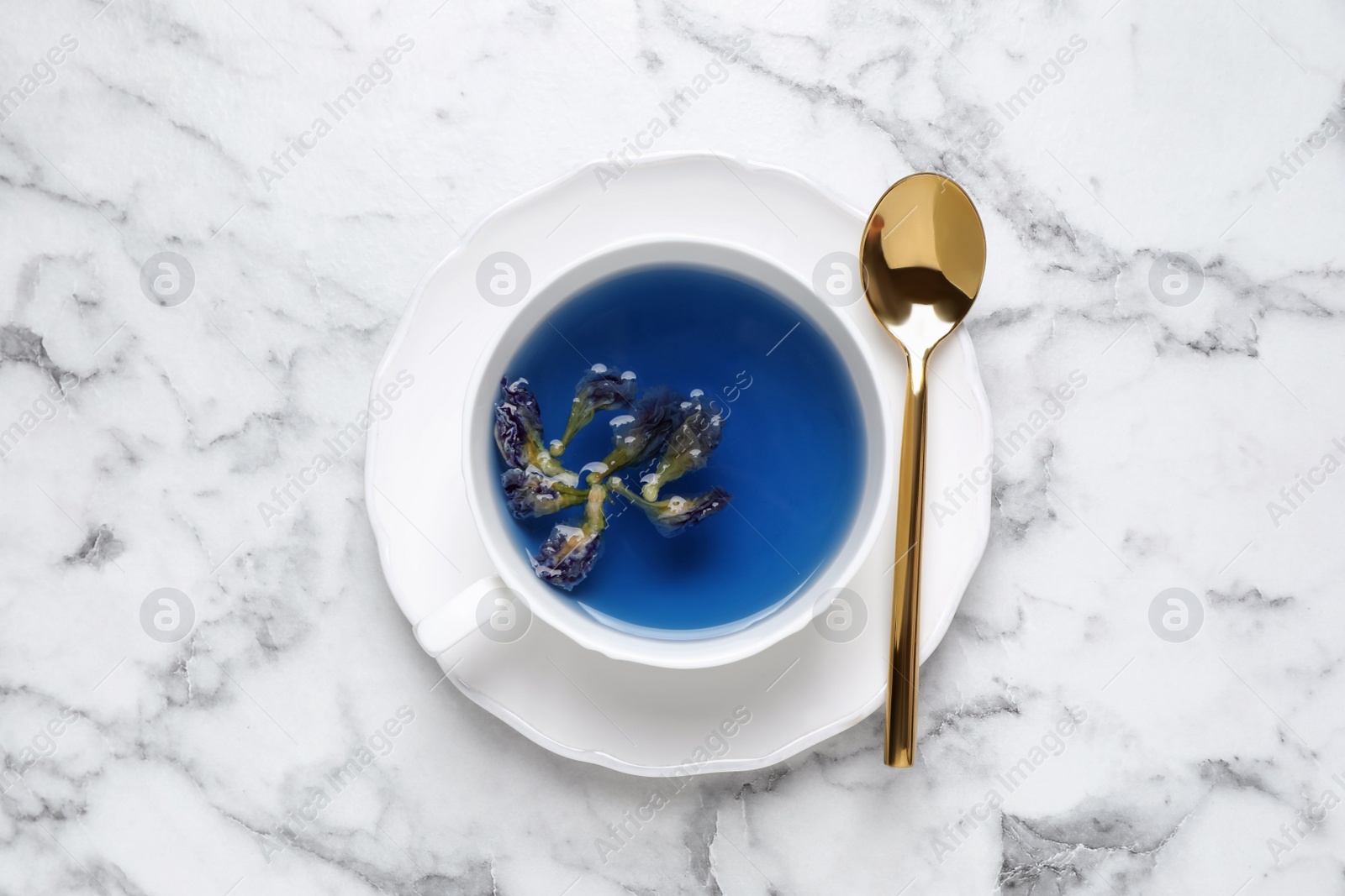 Photo of Organic blue Anchan in cup on white marble table, top view. Herbal tea