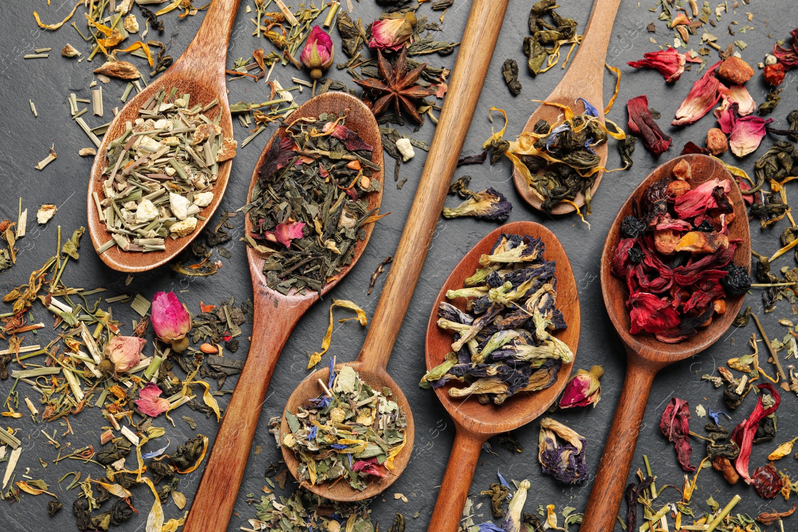 Photo of Wooden spoons with different teas on black table, flat lay