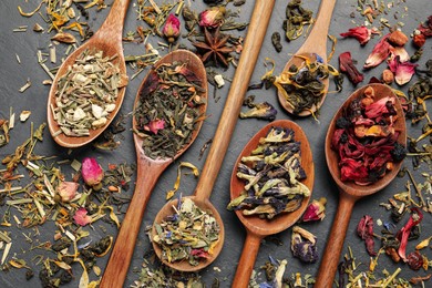 Wooden spoons with different teas on black table, flat lay