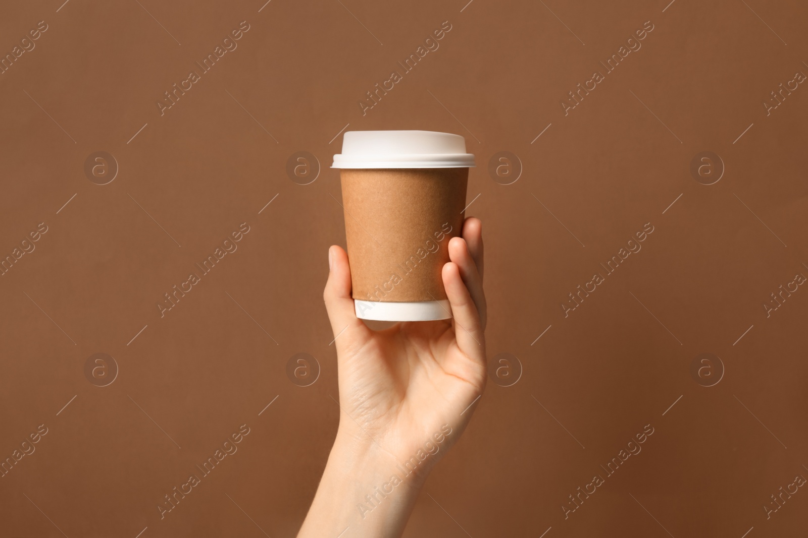 Photo of Woman holding takeaway paper coffee cup on brown background, closeup