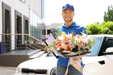 Delivery man with beautiful flower bouquet near car outdoors