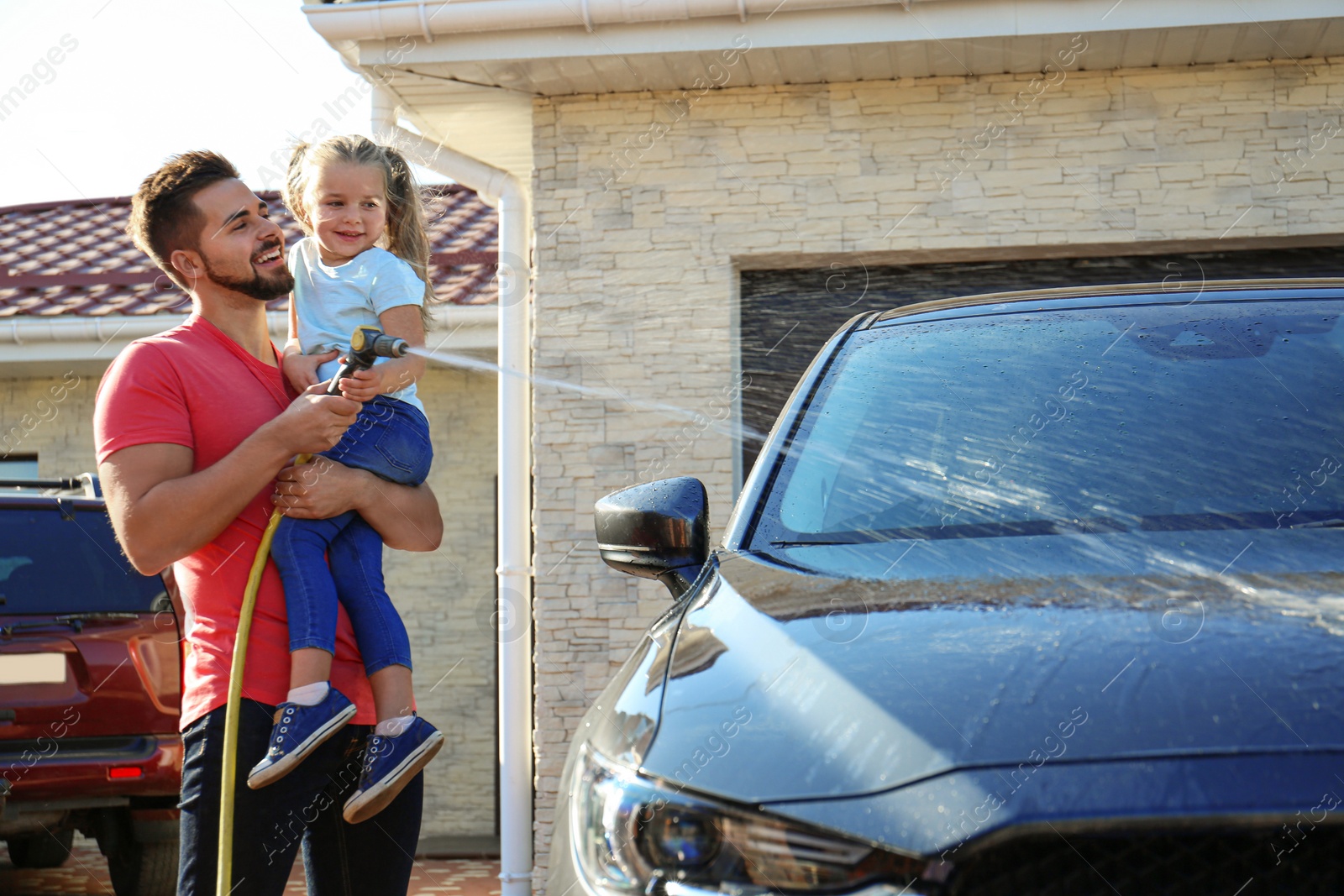 Photo of Dad and daughter washing car at backyard on sunny day