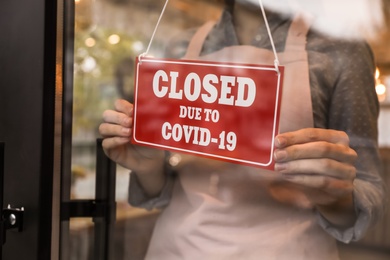 Photo of Woman putting red sign with words "Closed Due To Covid-19" onto glass door, closeup