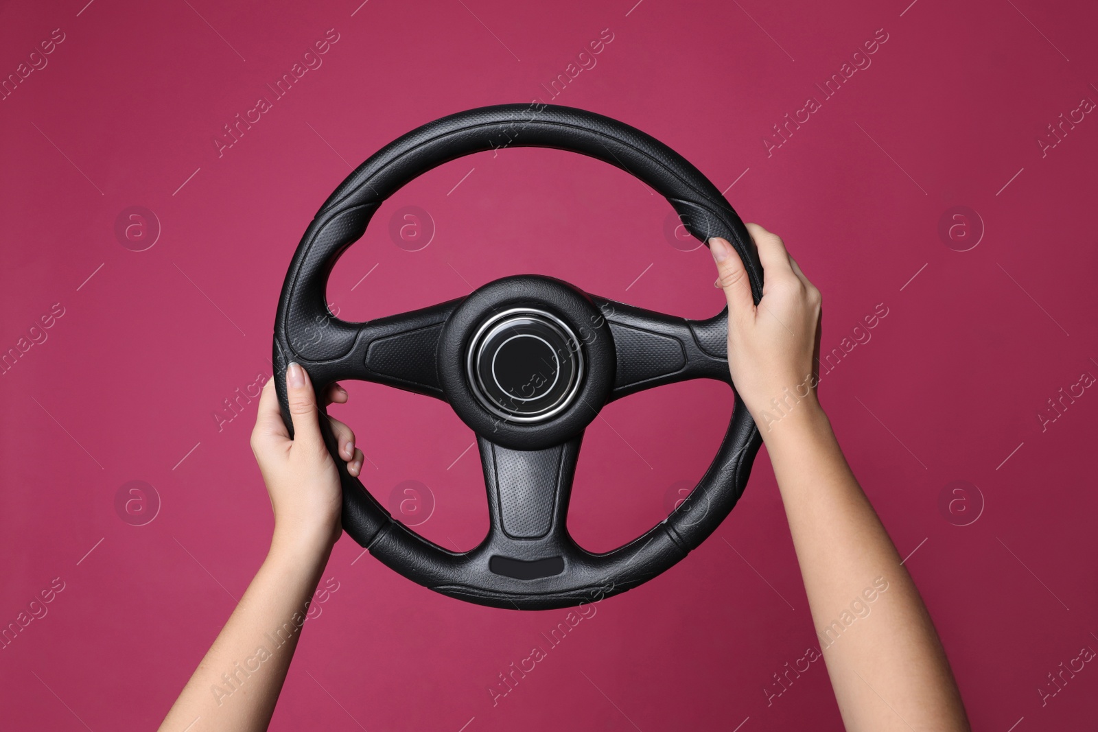 Photo of Woman holding steering wheel on crimson background, closeup