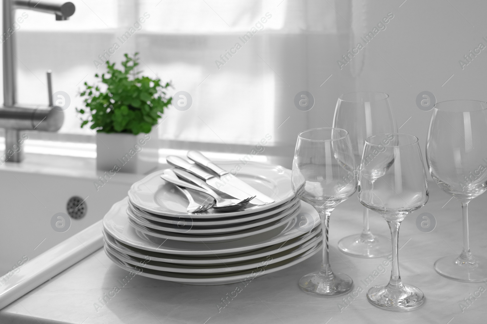 Photo of Different clean dishware, cutlery and glasses on countertop near sink in kitchen