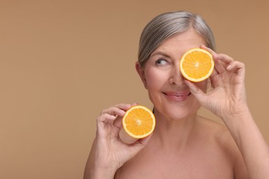 Photo of Beautiful woman with halves of orange rich in vitamin C on beige background, space for text