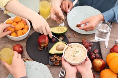 Photo of Friends eating vegetarian food at wooden table indoors, closeup