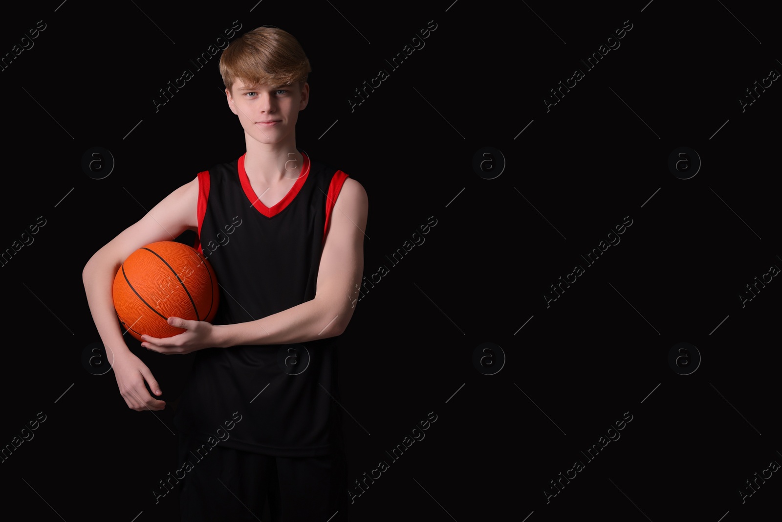 Photo of Teenage boy with basketball ball on black background. Space for text