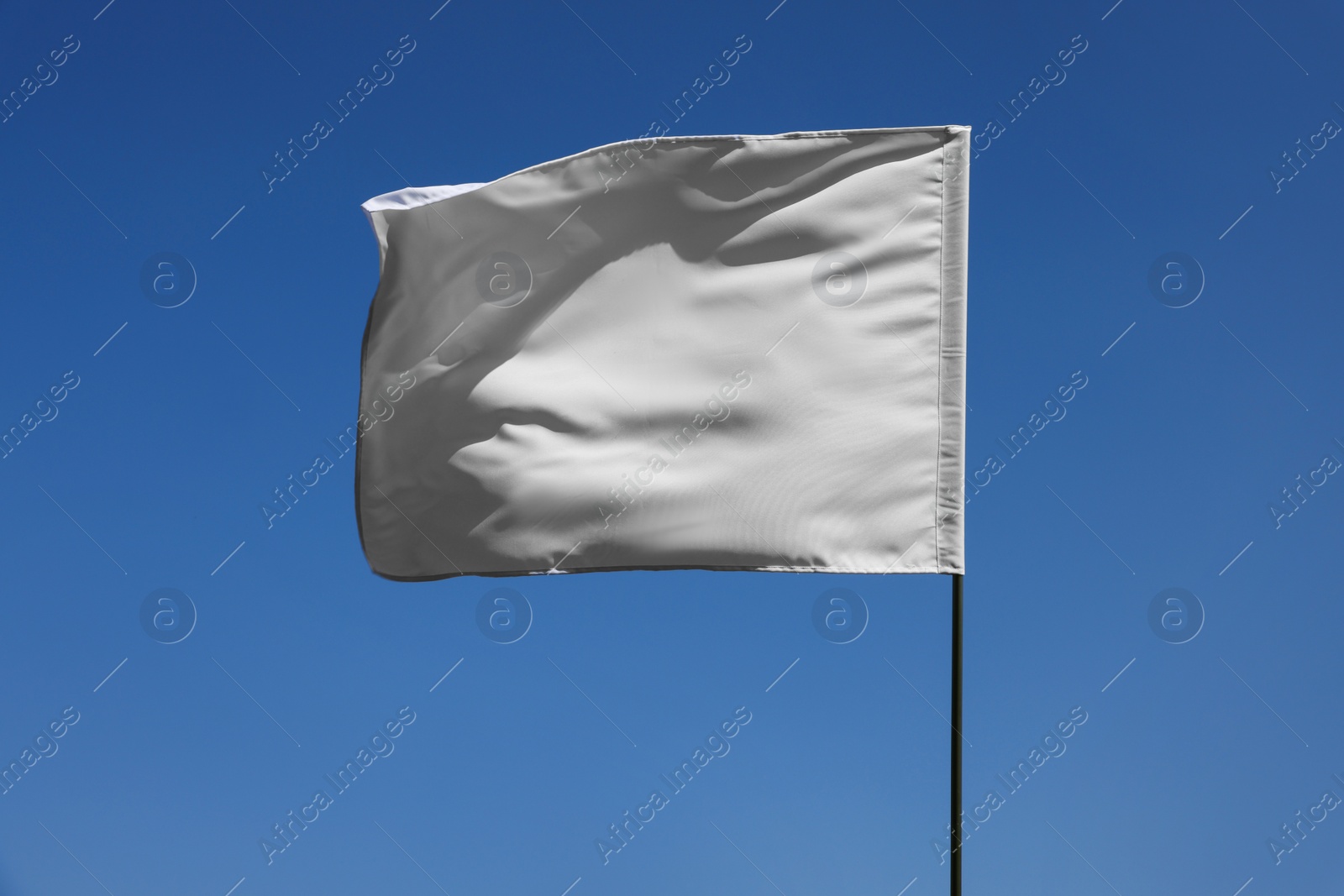 Photo of White flag fluttering against blue sky on sunny day