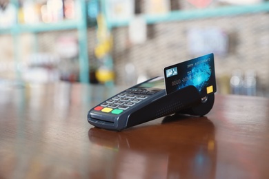 Photo of Credit card machine for non cash payment on wooden counter in cafe. Space for text