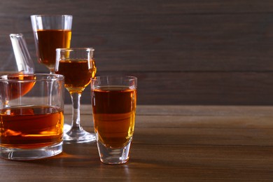 Photo of Different delicious liqueurs in glasses on wooden table, space for text