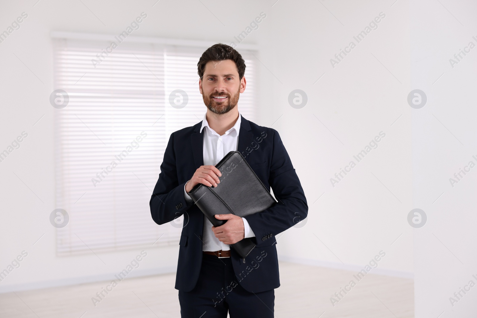 Photo of Happy real estate agent with leather portfolio in new apartment