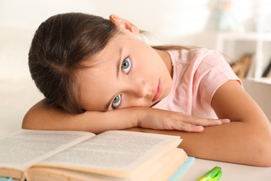 Photo of Bored little girl doing homework at table indoors