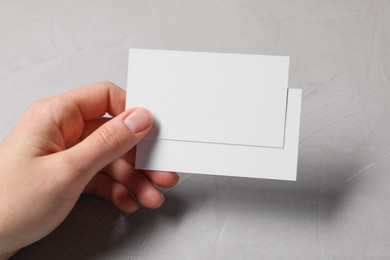 Woman holding blank cards at light grey table, closeup. Mockup for design