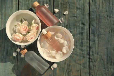 Bottles of rose essential oil and flowers on light blue wooden table, flat lay. Space for text