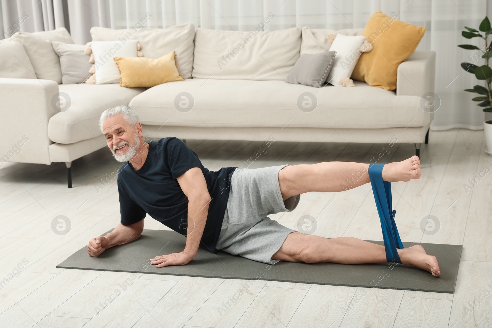 Photo of Senior man doing exercise with fitness elastic band on mat at home