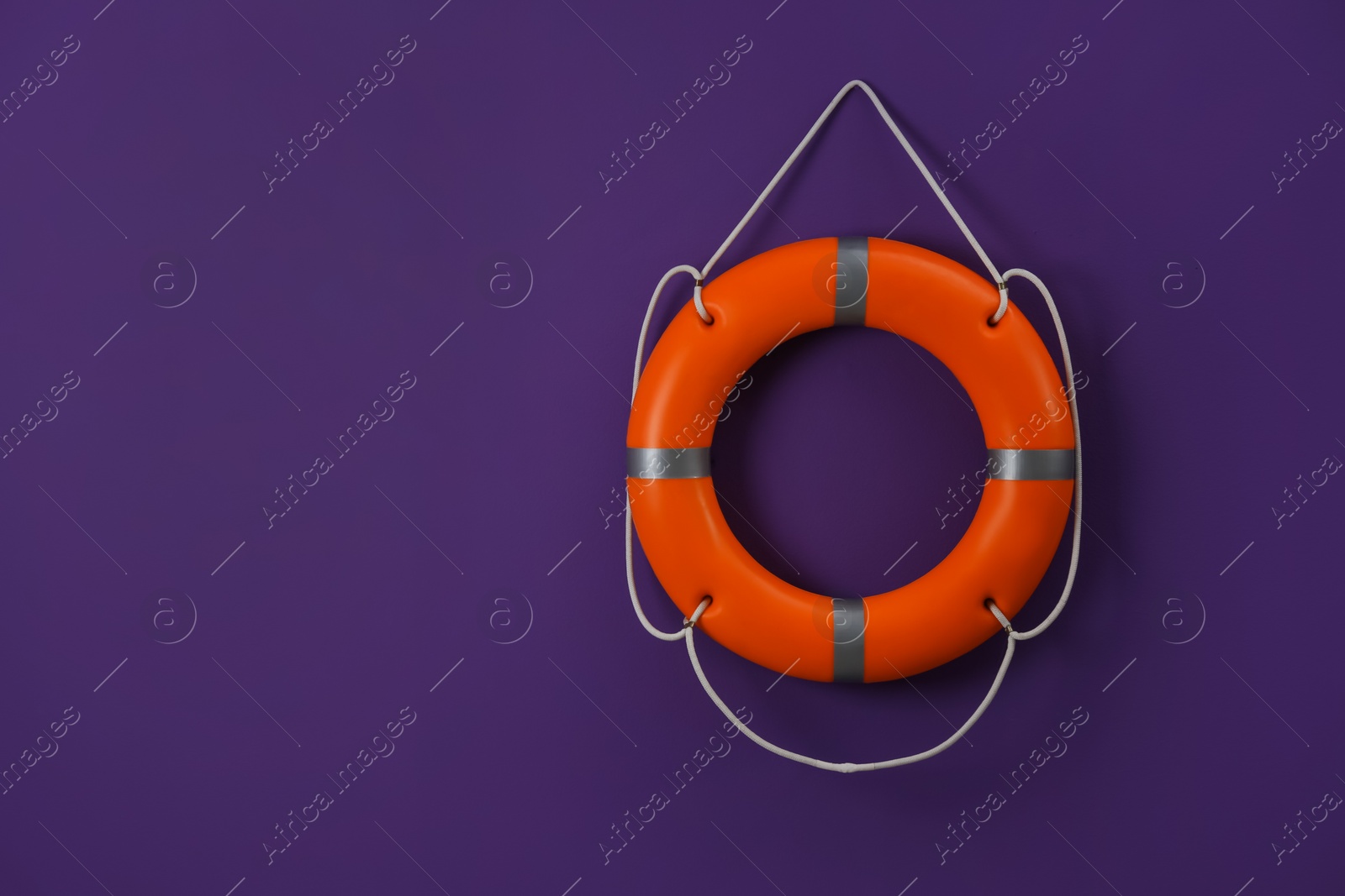 Photo of Orange lifebuoy and space for text on violet background. Rescue equipment